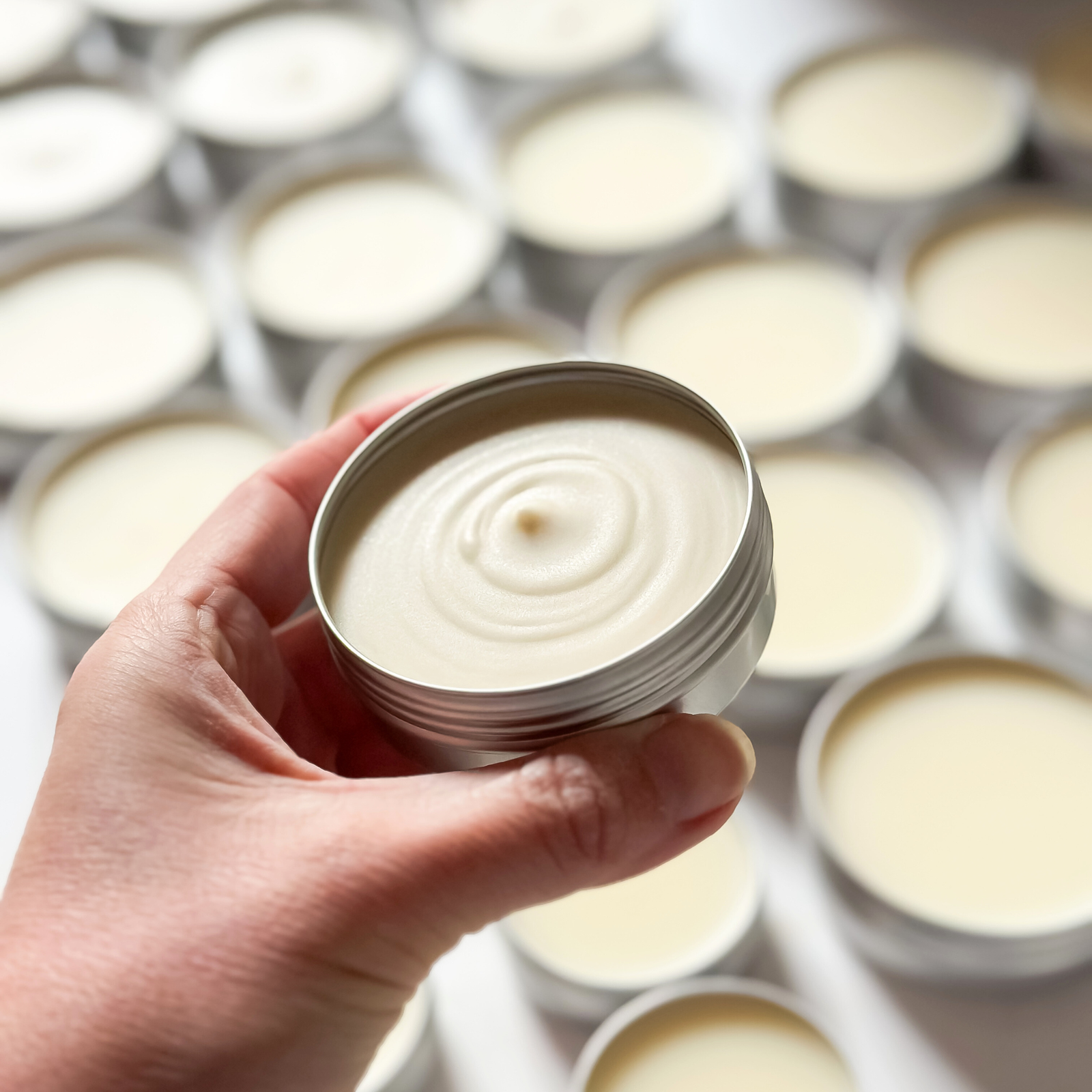 Hand holding a freshly poured CONCHUS natural deodorant tin, surrounded by rows of plastic-free handmade skincare.